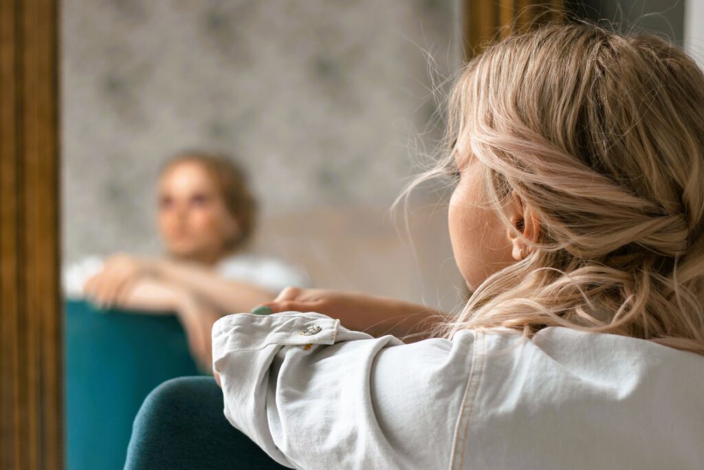 Femme assise observant son reflet dans un miroir, symbole du temps d'observation et d'exploration nécessaire concernant son évolution professionnelle.
